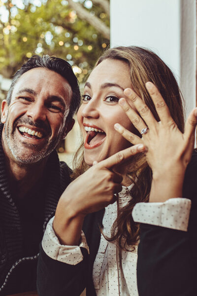 Affectionate couple announcing their engagement with selfies while sitting at cafe. Happy couple taking a selfie and showing off their wedding ring at coffee shop.
